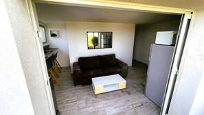 Ein gemütlicher Wohnraum mit einer Couch, einem kleinen Tisch, einem Kühlschrank und einem Fenster mit Blick.