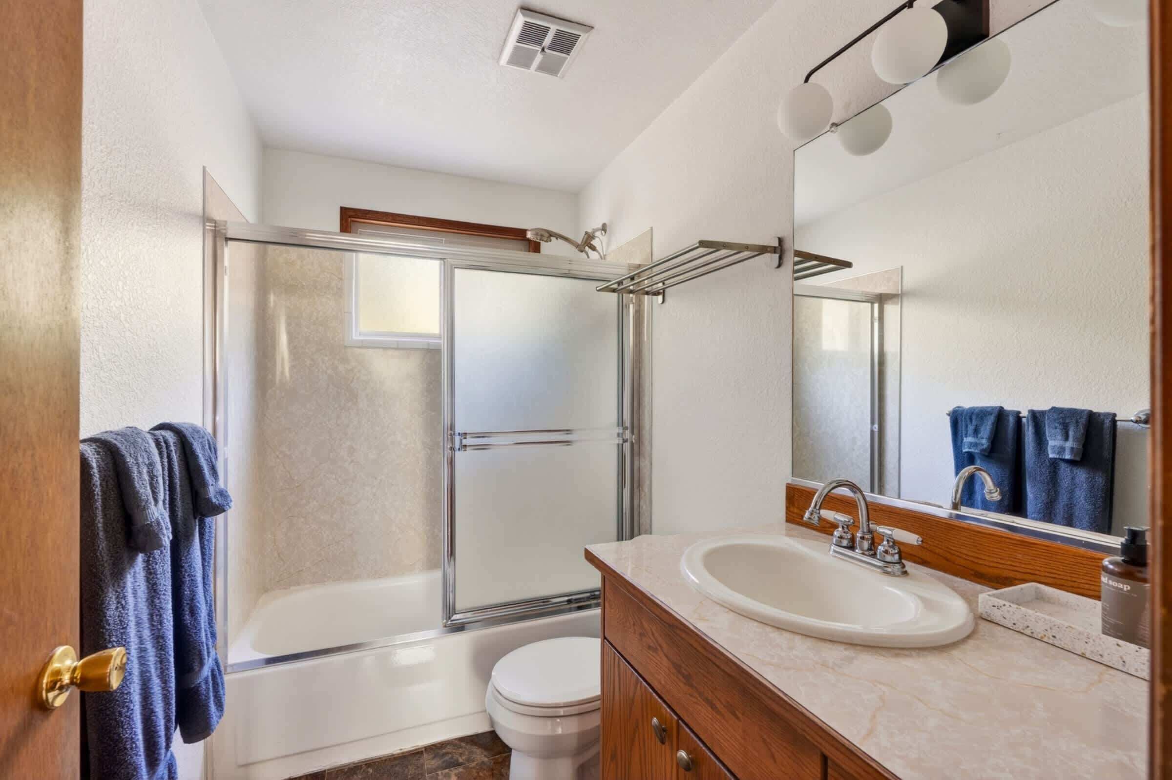 Une salle de bain avec une douche à parois de verre, des toilettes blanches, un lavabo avec un miroir et un porte-serviettes avec des serviettes.