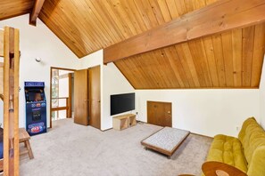 Ein Zimmer mit schrägem Dach, einem Fernseher, einer Couch, einem kleinen Tisch und einem Holzkabinett.