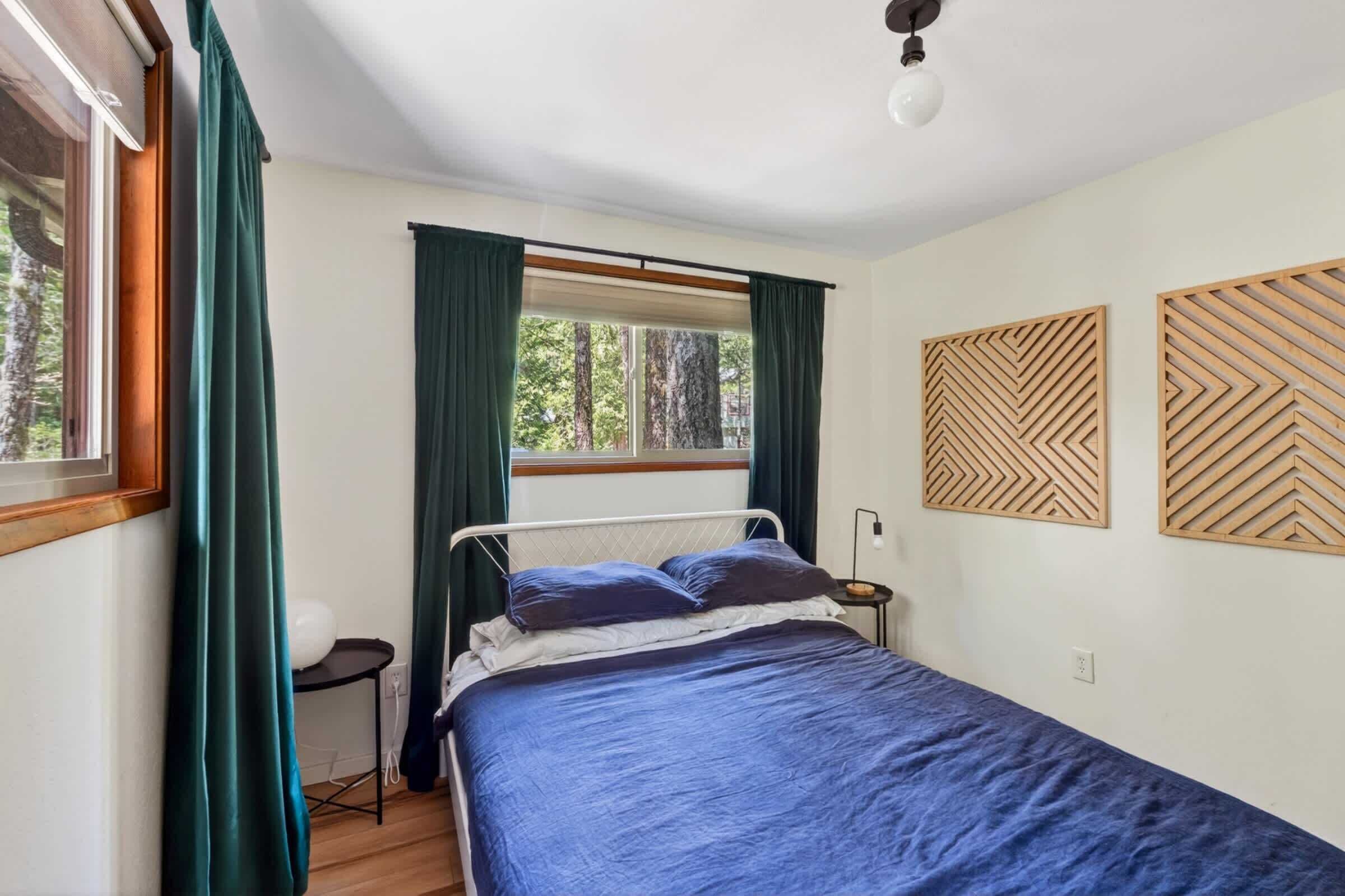 A bedroom with a bed, a window with curtains, a bedside table, and wall art.