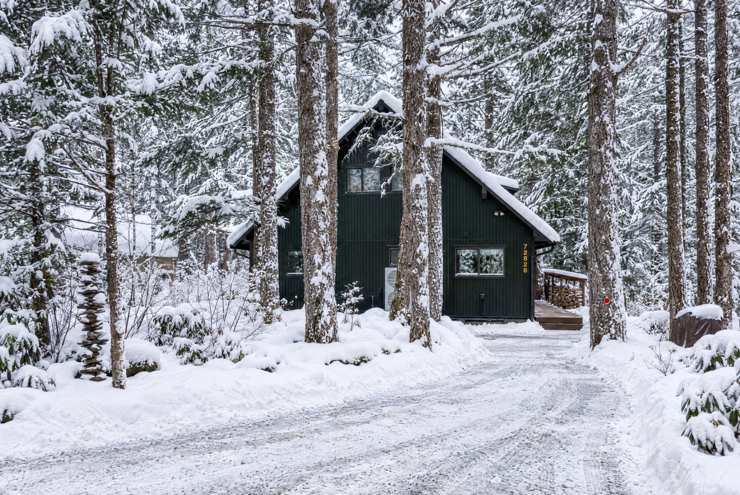 Une cabane dotée d’un toit à forte pente, entourée d’arbres couverts de neige.