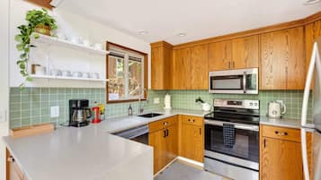 A modern kitchen with wooden cabinets, stainless steel appliances, and a green tiled backsplash.