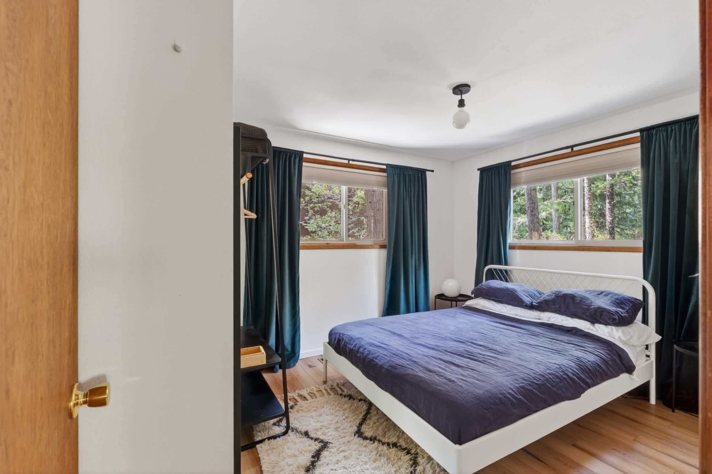 Ein Schlafzimmer mit einem Bett, einem Nachttisch, einer Lampe und einem Fenster mit Vorhängen.