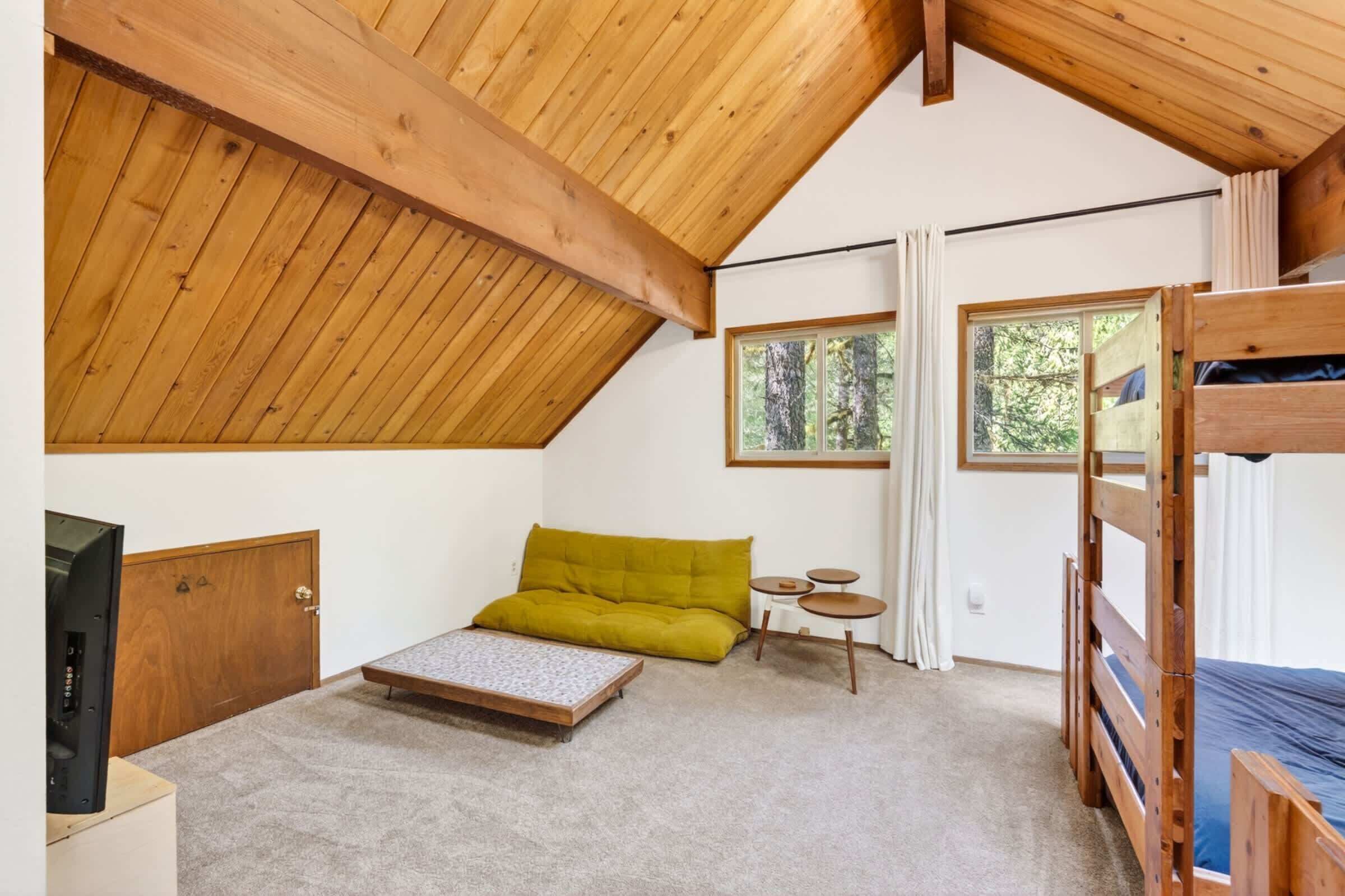 A room with a sloped ceiling, a bunk bed, a sofa, a small table, and a television.