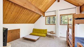 A room with a sloped ceiling, a bunk bed, a sofa, a small table, and a television.