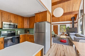 Una cocina moderna con armarios de madera, electrodomésticos de acero inoxidable y un amplio ventanal con vistas a una sala de estar con chimenea.