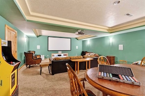A room with a projector screen, a couch, a dining table, and a vintage arcade machine.