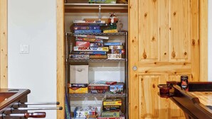 A room with a wooden door, a shelf with board games, and a table with a pool cue.