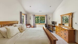 A bedroom with a bed, a desk, a chair, a dresser, and a window with curtains.