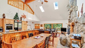 A spacious kitchen with wooden cabinets, a dining area with a wooden table and chairs, a stone accent wall, and a large window providing natural light.