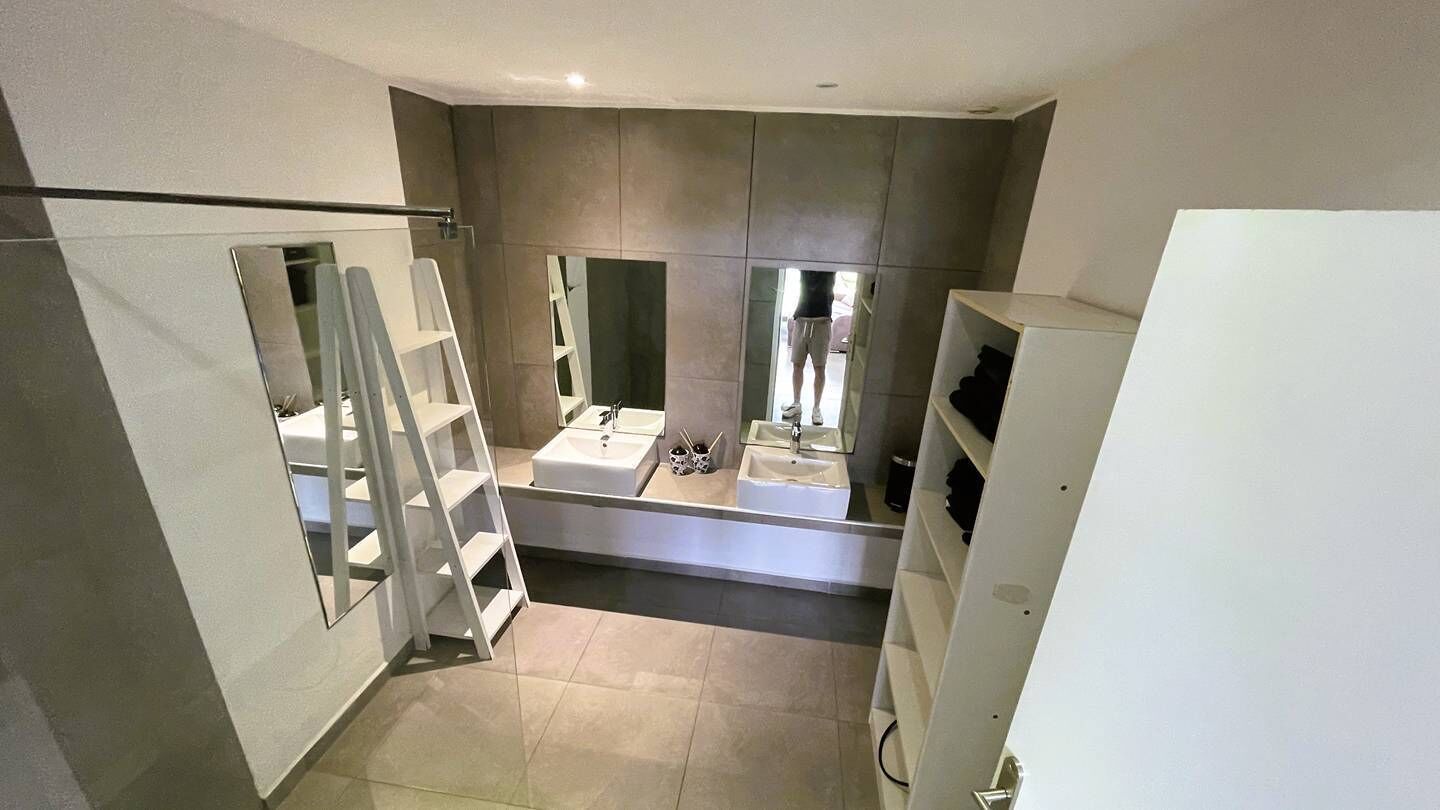 Une salle de bain moderne avec une douche à l’italienne, un grand miroir et un meuble-lavabo blanc.