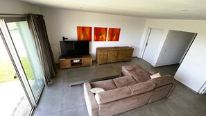 A modern living room with a sofa, TV, wooden cabinet, and artwork on the wall. - Appartement Pascialella, 7 pers, piscine chauffée, vue mer (PORTO VECCHIO)