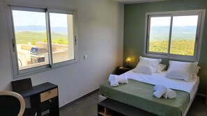 Ein Schlafzimmer mit einem Bett, zwei Fenstern, einem Schreibtisch und einem Stuhl.