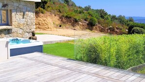 A patio with a hot tub, a stone wall, and a view of a hillside. - Domaine Pascialella, 20 pers, 3 piscines, vue mer (PORTO VECCHIO)