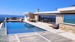 A modern outdoor pool area with a wooden deck, stone walls, and a dining set. - Domaine Pascialella, 20 pers, 3 piscines, vue mer (PORTO VECCHIO)