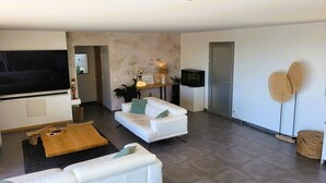 A modern living room with a flat-screen TV, white sofas, a wooden coffee table, and a wall-mounted TV. - Domaine Pascialella, 20 pers, 3 piscines, vue mer (PORTO VECCHIO)