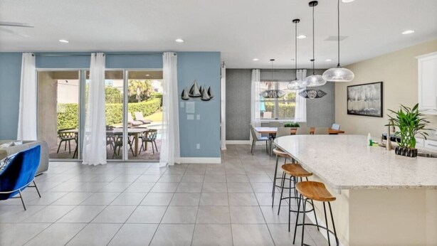 A modern kitchen with a large island, bar stools, pendant lights, and a dining area with a table and chairs. - Family Vacation Home Near Disney - Pool & Spa (Kissimmee)