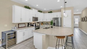 A modern kitchen with white cabinets, stainless steel appliances, a granite countertop, and a central island with bar stools. - Family Vacation Home Near Disney - Pool & Spa (Kissimmee)