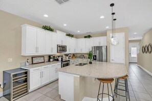Uma cozinha moderna com armários brancos, eletrodomésticos de aço inoxidável, bancada de granito e uma ilha central com banquetas.