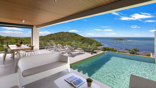 Uma área moderna de piscina ao ar livre com vista para o mar e uma paisagem montanhosa.