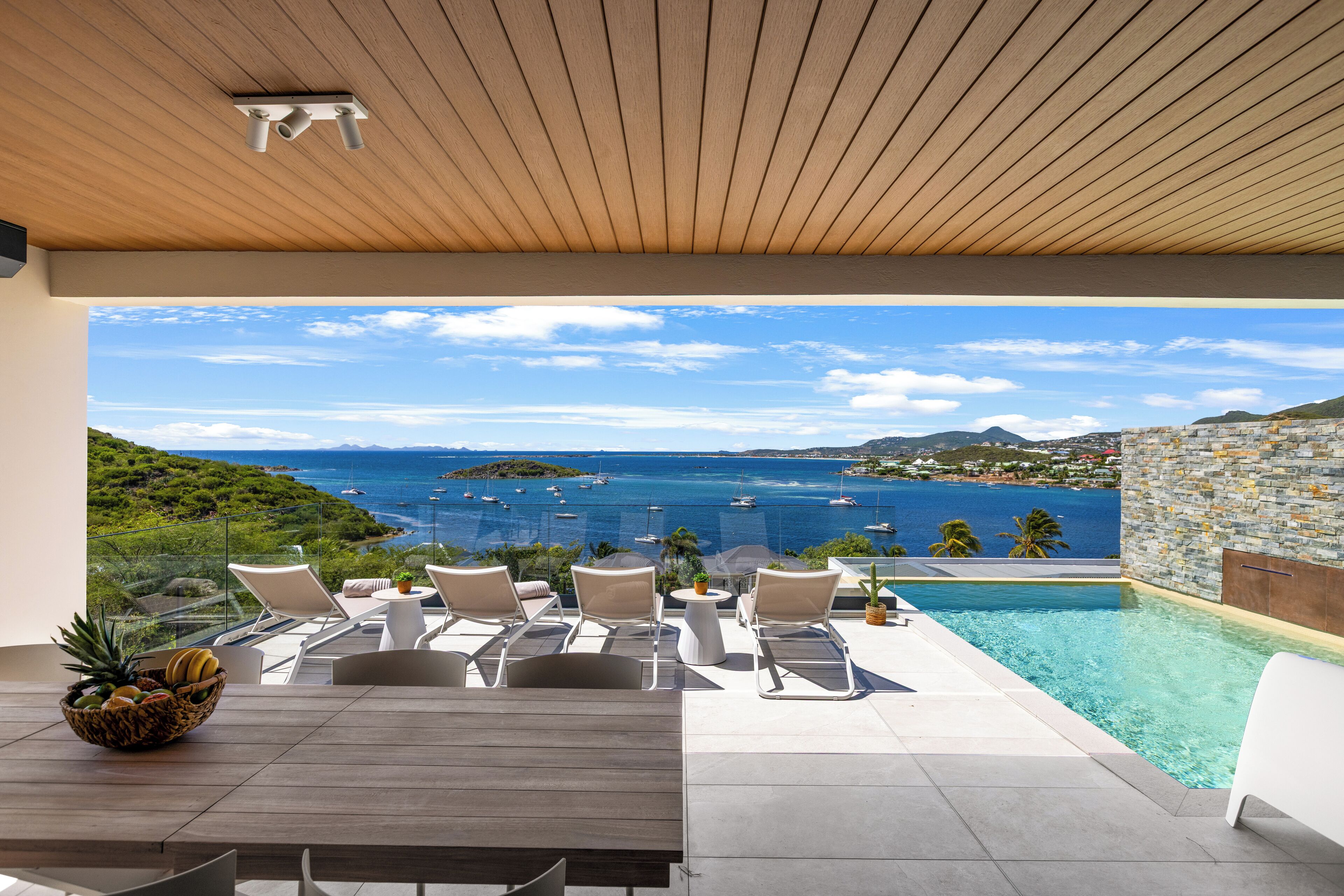 En moderne udendørs terrasse med pool, liggestole og havudsigt.