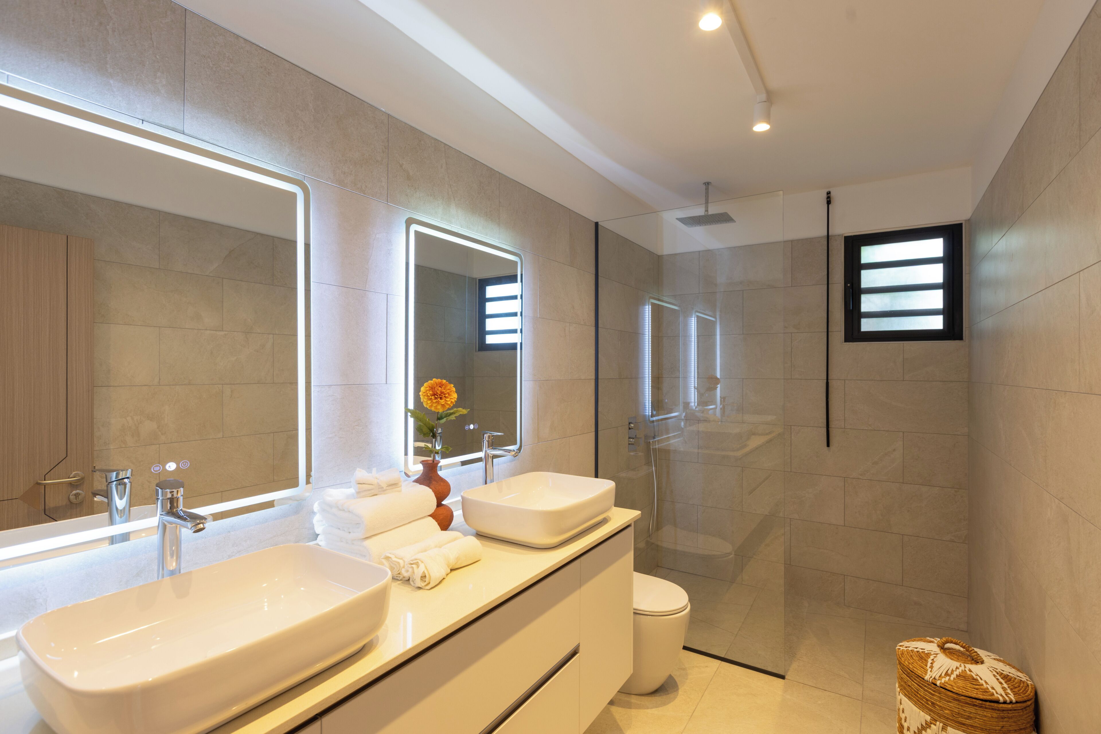 Une salle de bain moderne avec deux lavabos, des toilettes, une douche et un grand miroir.