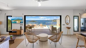 A modern living room with a large TV, comfortable seating, a ceiling fan, and a view of the sea. - Villa Soléro, facing the turquoise waters of St Martin, opposite St Barthélémy. (Saint Martin)