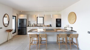 Uma cozinha moderna com ilha central, banquetas, geladeira e área de jantar.