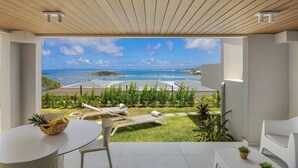 Uma varanda com vista para o mar, uma mesa com uma cesta de frutas e duas cadeiras de descanso.