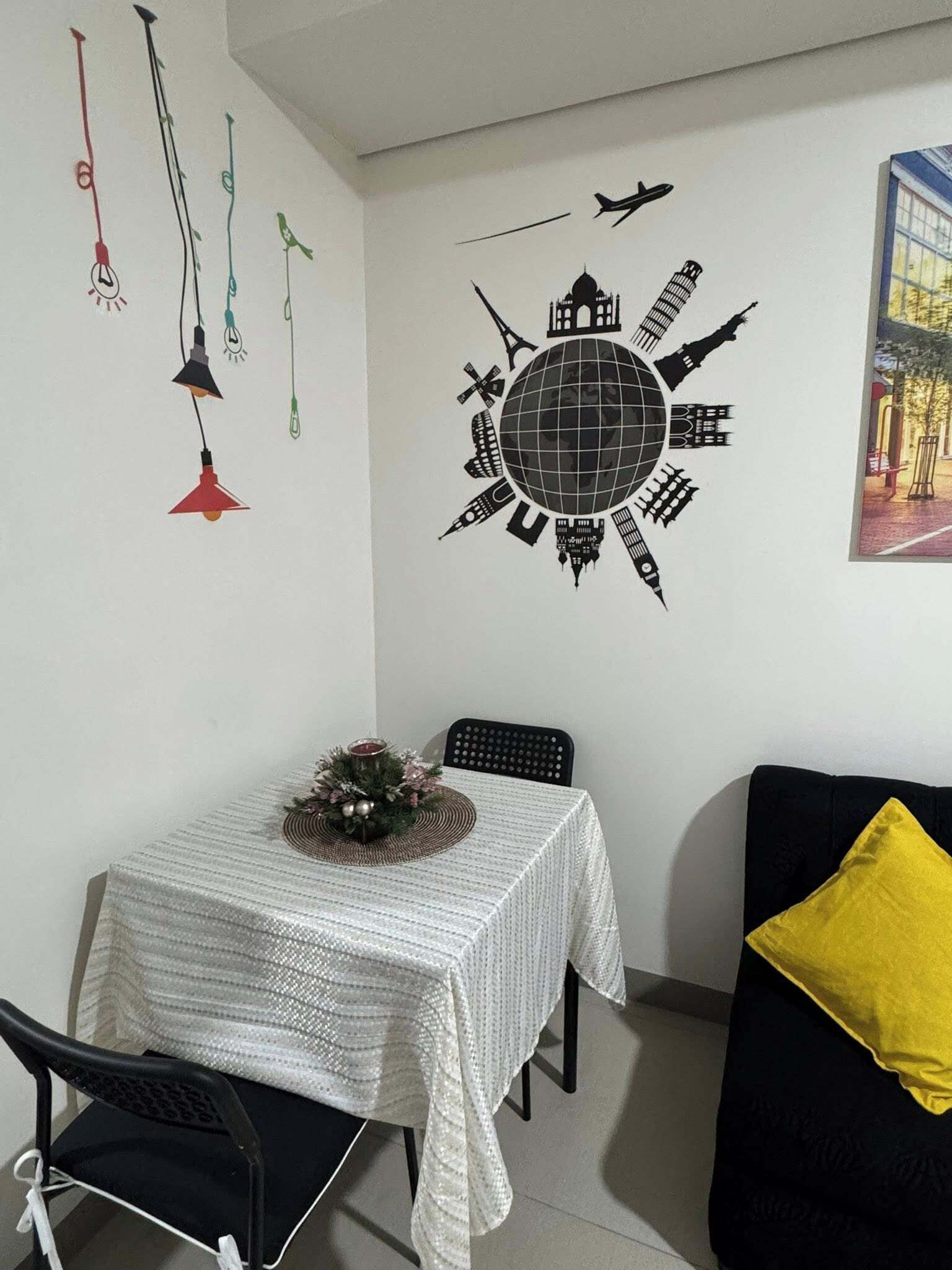 Un coin repas comprenant une table, des chaises, une décoration murale représentant un globe terrestre et un coussin jaune sur un canapé noir.
