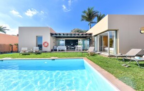 Ein modernes Haus mit Swimmingpool, Sitzgelegenheiten im Freien und einer überdachten Terrasse.