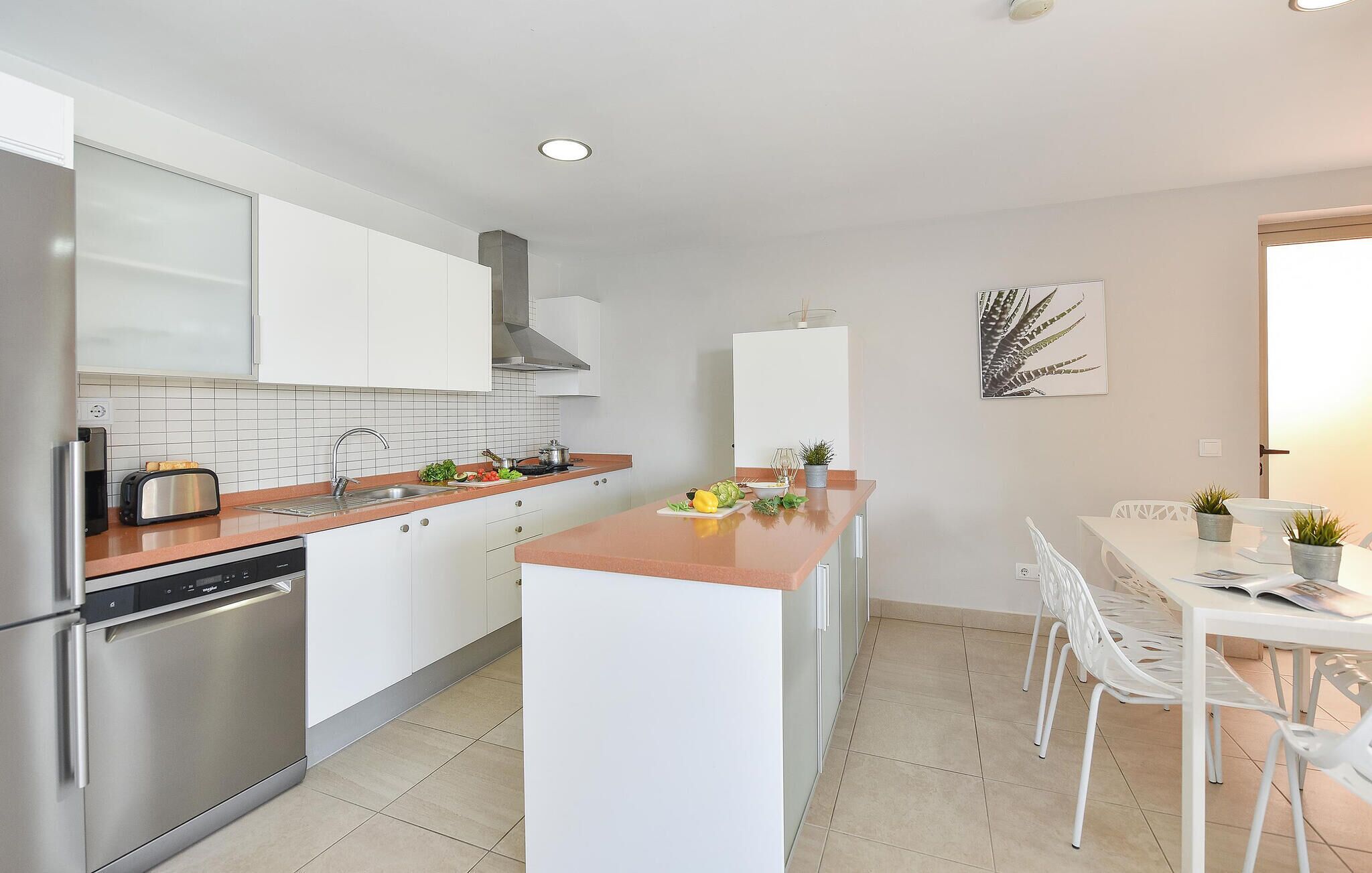 Una cocina moderna con electrodomésticos de acero inoxidable, armarios blancos y una isla central con pileta.
