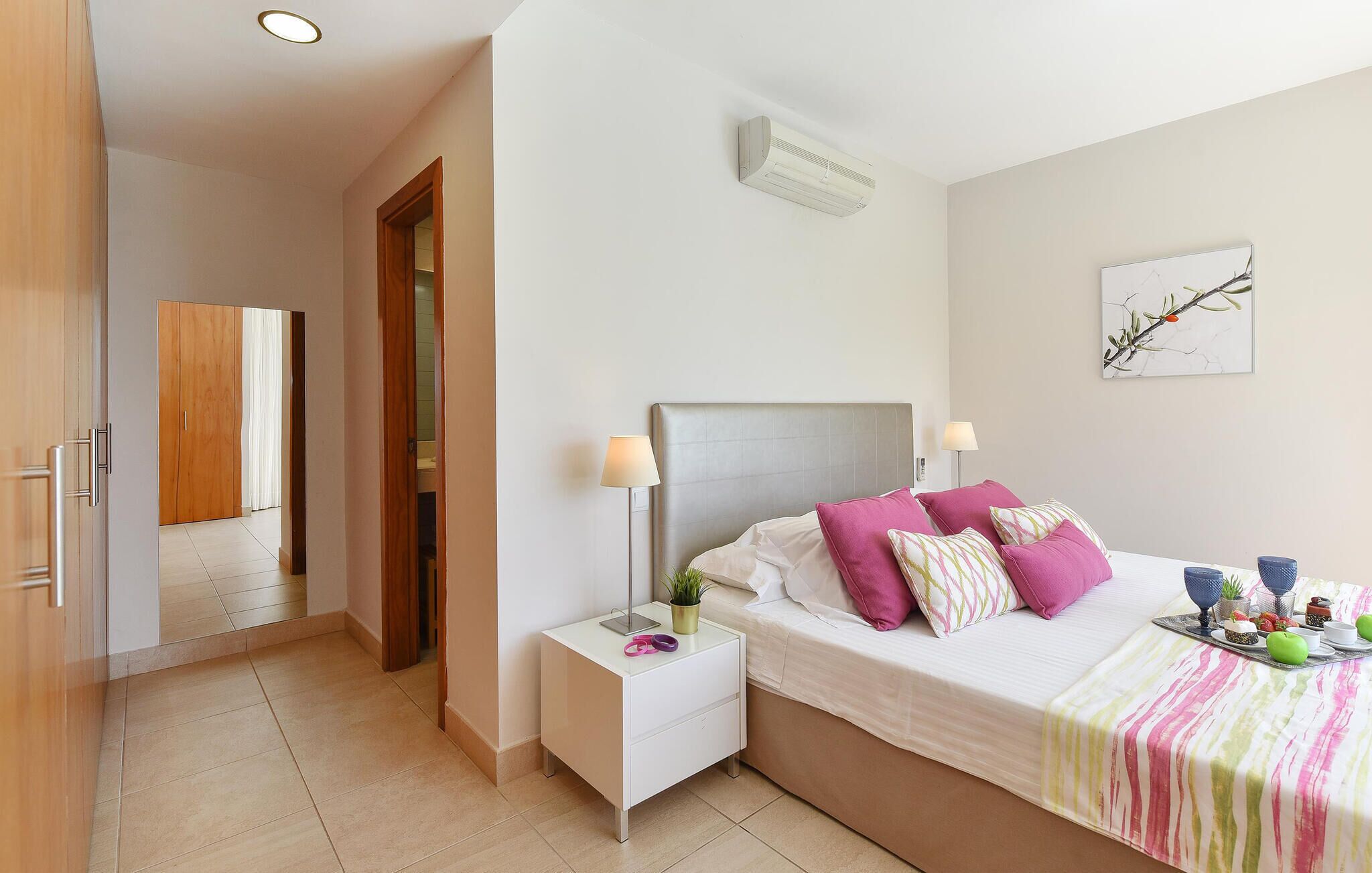 Ein Schlafzimmer mit Bett, Nachttischen, einer Wand-Klimaanlage, einer Tür und einem Flur.