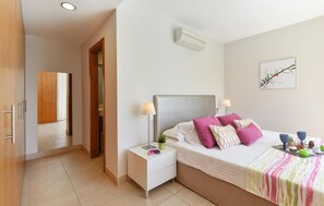 Ein Schlafzimmer mit Bett, Nachttischen, einer Wand-Klimaanlage, einer Tür und einem Flur.