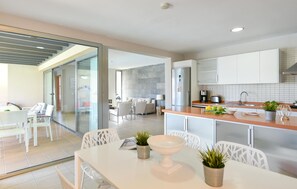 Eine moderne Küche mit weißen Schränken, einem Edelstahlkühlschrank und einer Essecke mit weißen Stühlen und einem Tisch.