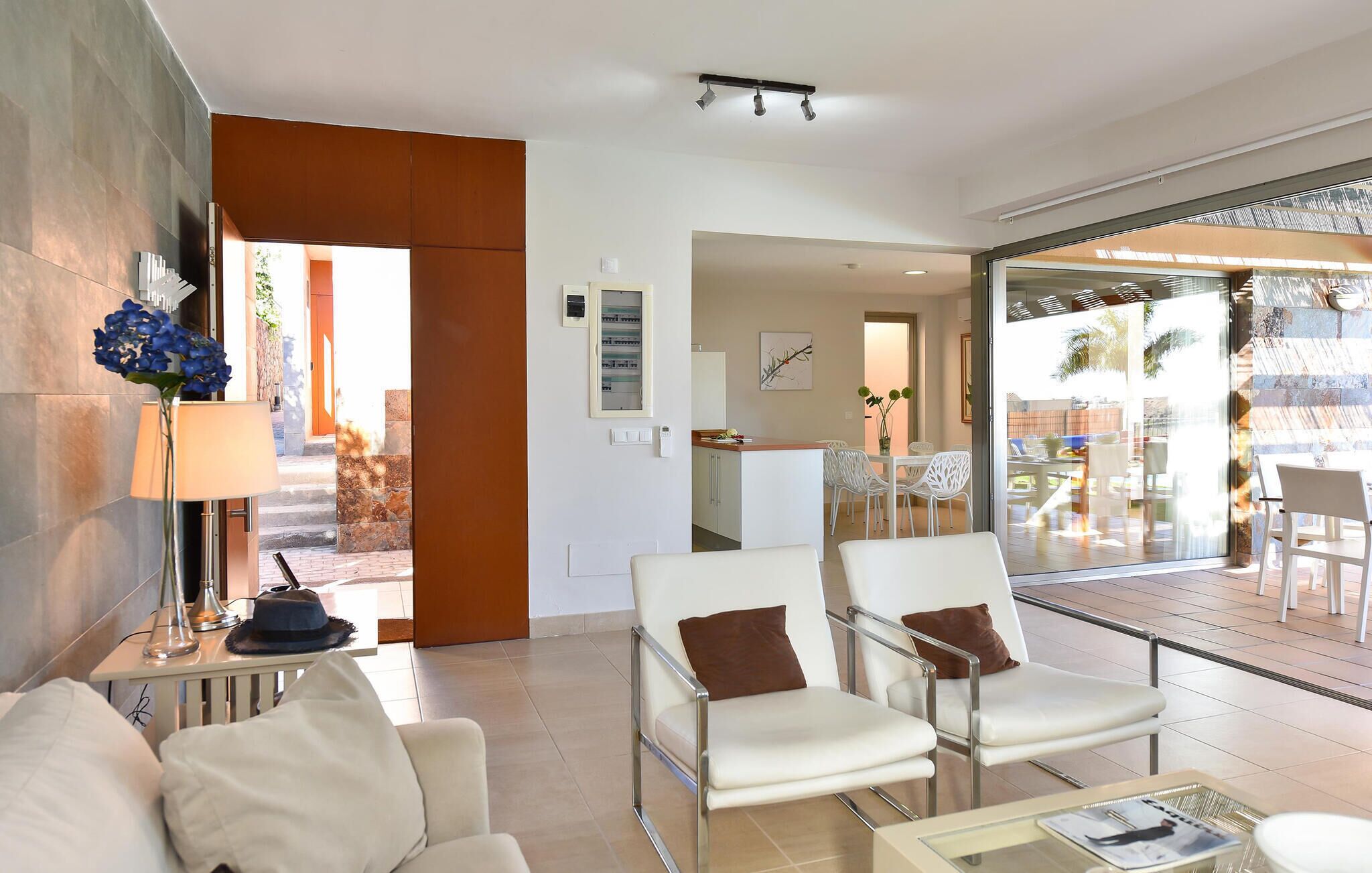 A modern hotel room with a seating area, a glass door leading to an outdoor patio, and a visible kitchen area.