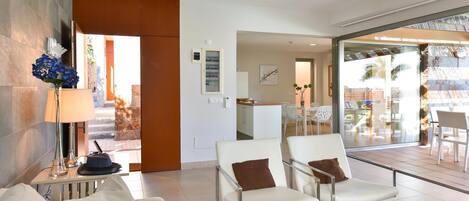 A modern hotel room with a seating area, a glass door leading to an outdoor patio, and a visible kitchen area.