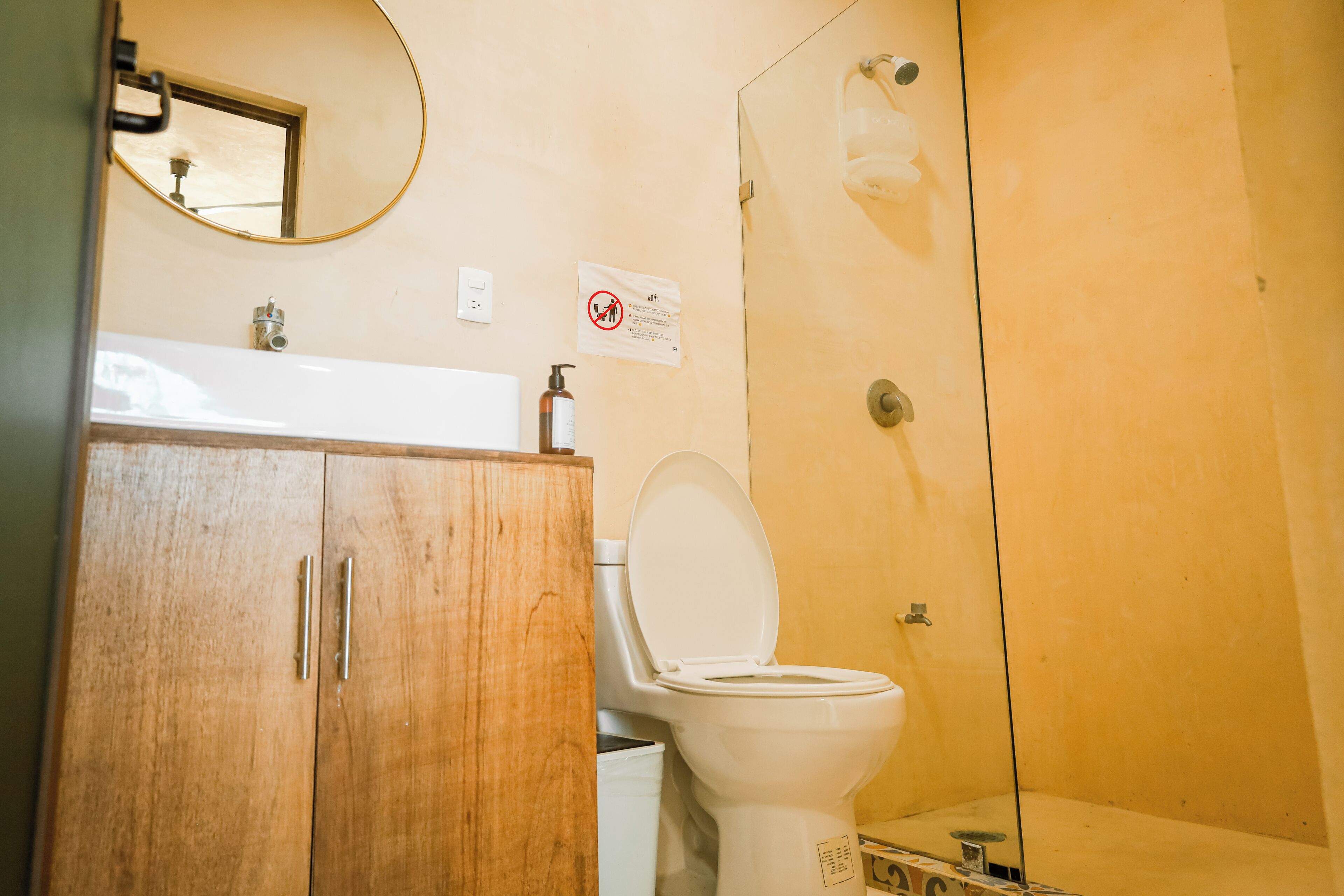 Une salle de bain avec un meuble en bois, un lavabo blanc, des toilettes et une cabine de douche en verre.