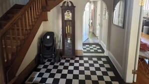 Eine Treppe mit Holzhandläufen führt zu einem Flur mit schachbrettartigem Boden in Schwarz und Weiß.
