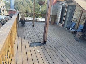 Una terraza de madera con barandilla metálica, plantas en macetas y mobiliario exterior.