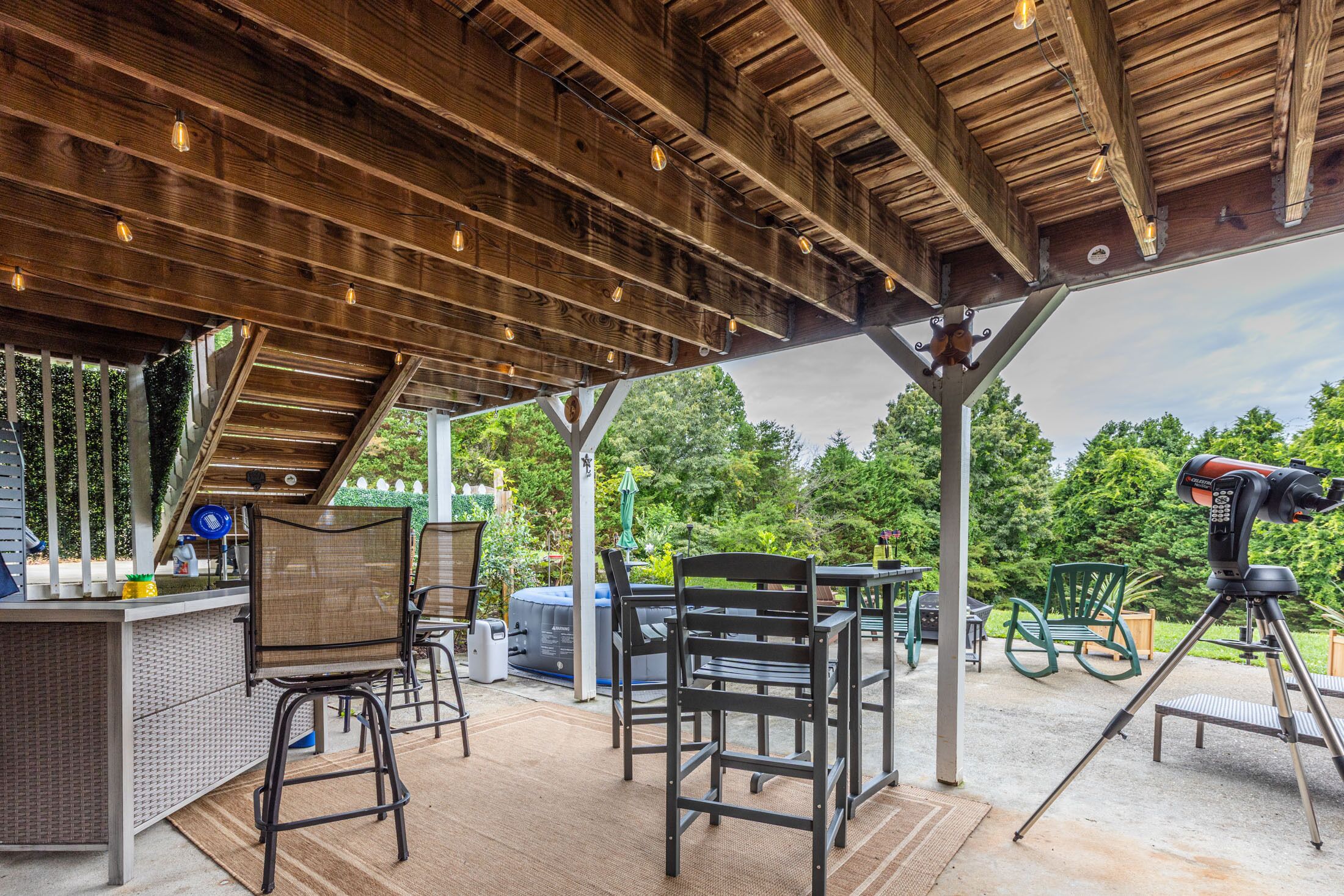 Un espace extérieur aménagé en terrasse, avec un plafond en bois, des sièges, un barbecue et un télescope.