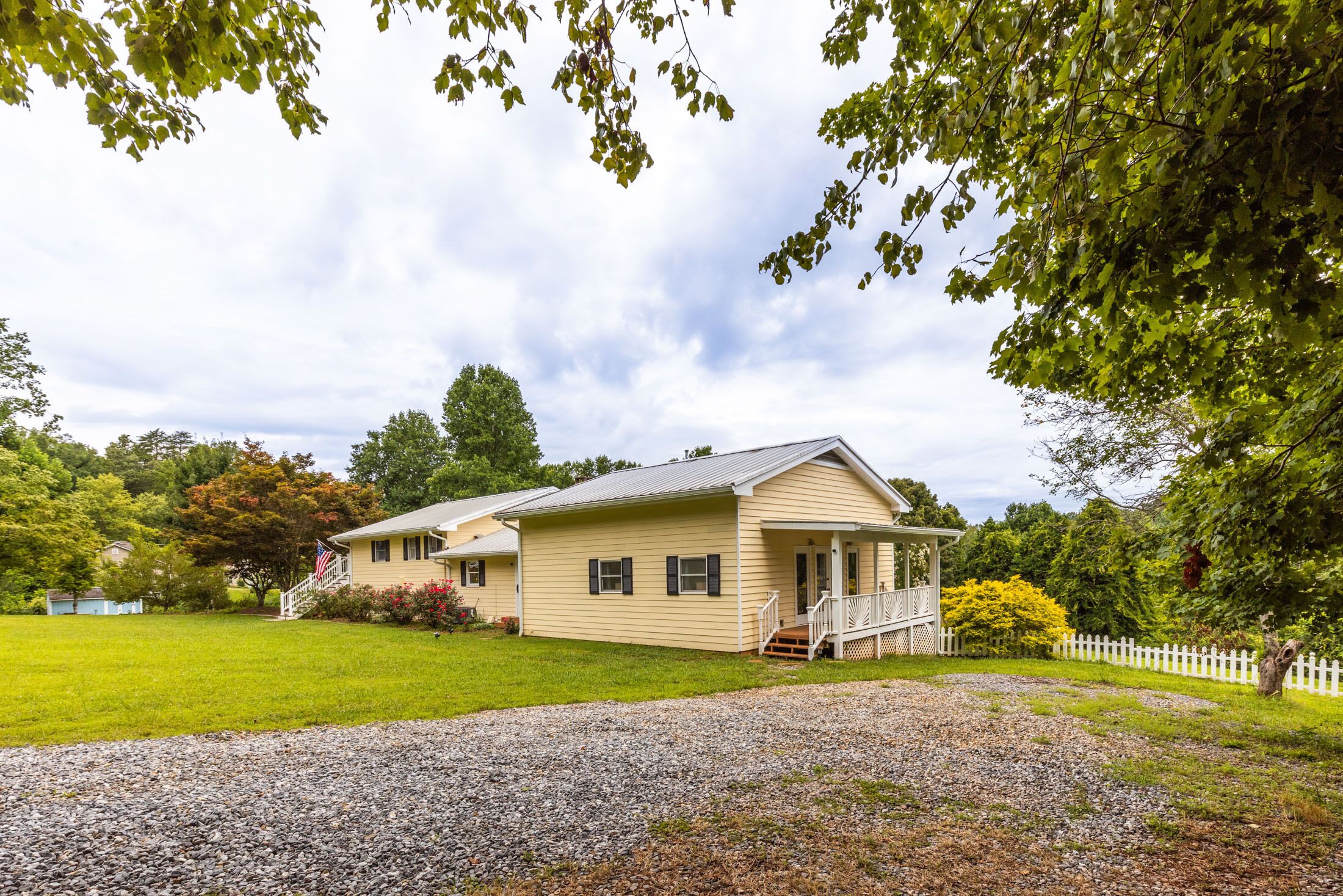 A single-story house with a porch, a front yard with a gravel path, and a white picket fence.