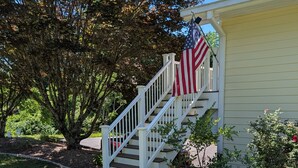 A house with a white staircase leading to a porch, an American flag, and a tree with autumn leaves.