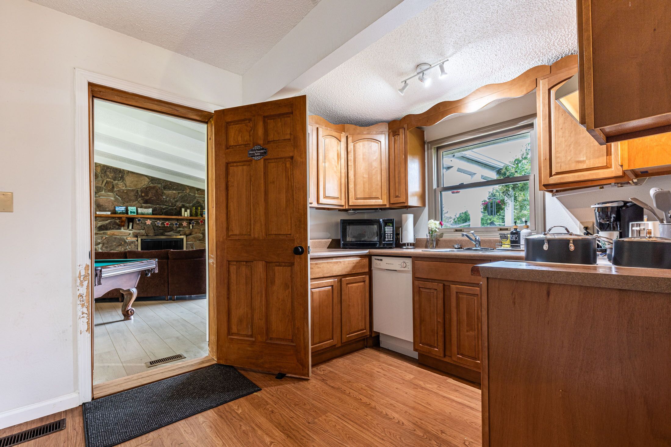 A kitchen with wooden cabinets, a microwave, a dishwasher, and a window with a view of greenery.