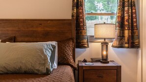 A bed with a quilted cover, a bedside lamp, a clock, and a nightstand with drawers.