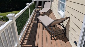 A wooden deck with two chairs and a table, a white railing, and a house with beige siding.