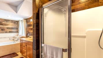 Une salle de bain avec une douche, une baignoire, un lambris en bois, un lavabo et une serviette accrochée à la porte.