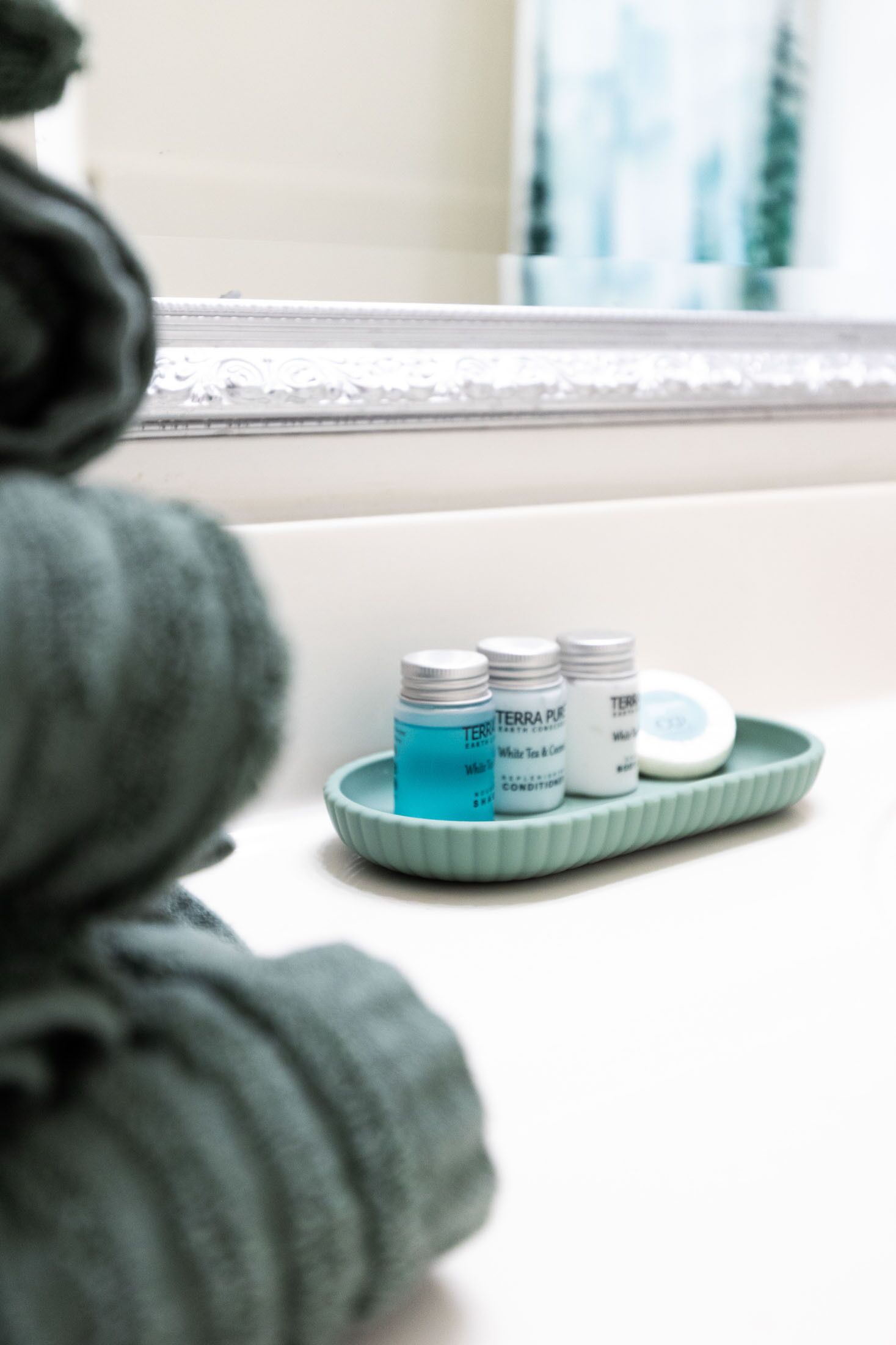 A bathroom with a white sink, a green soap dish, and two bottles of white soap.