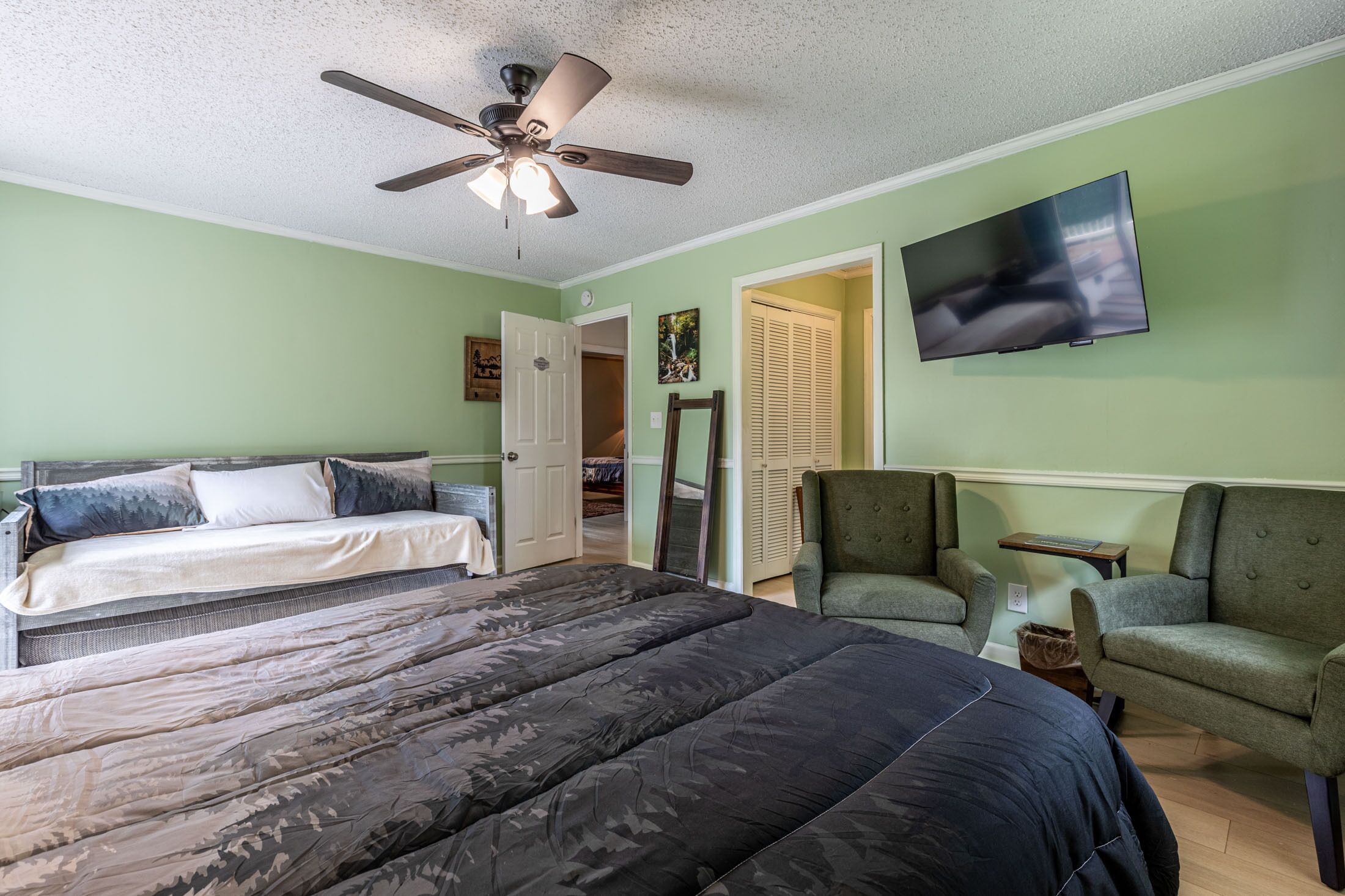 Un dormitorio con dos camas, un ventilador de techo, un televisor y un sillón verde.