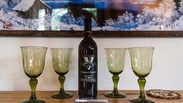 Une bouteille de vin rouge géorgien de la marque Vintner's Stache, accompagnée de quatre verres à vin verts, posée sur une surface en bois.